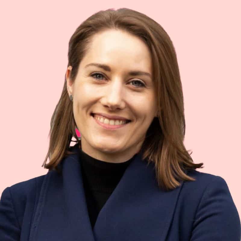 Nina Jameson lacht in die Kamera. Der Hintergrund ist pastelrot