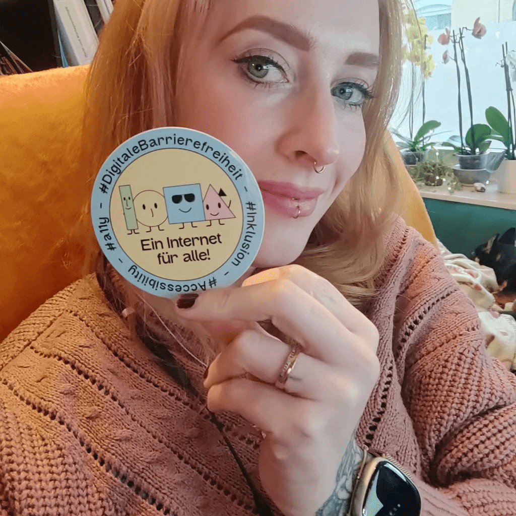 Marie hat den digitalen Barrierefreiheit-Sticker in der Hand und lächelt in die Kamera